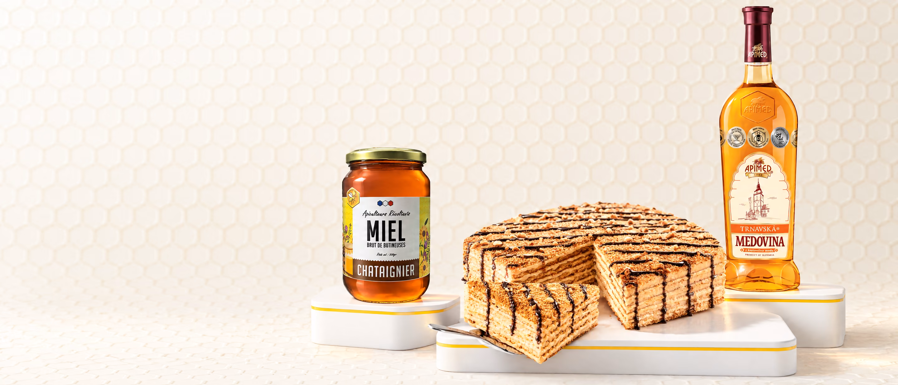 Un pot de miel de châtaignier, un gâteau au miel Marlenka entamé et une bouteille de vin de miel Apimed